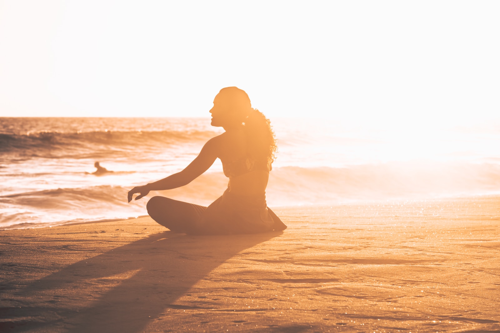 silhueta de mulher sentada à beira-mar durante o pôr do sol